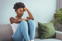 Femme malheureuse, seule et déprimée chez elle ; elle est assise sur le canapé et cache son visage dans un oreiller ; concept de dépression. Psychologie, solitude et personnes