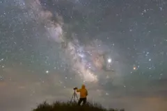 Pessoa observa o céu estrelado ao lado de um telescópio