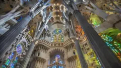 Interior da Sagrada Família com vários vitrais. É dia, então a luz brilha através deles, lançando raios multicoloridos, incluindo verde e amarelo