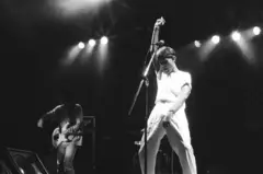 Cazuza erguendo um braço no palco; atrás, vê-se guitarrista