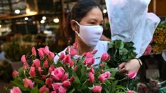 A woman wearing a mask carrying flowers in Hanoi