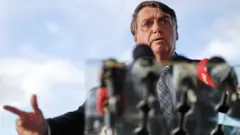 Bolsonaro dá entrevista em área externa, com vários microfones no palanque