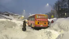 Автобус посреди снежных заносов, на фоне люди идут по неровным тропинкам.