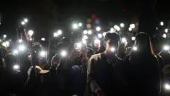 Un grupo de espectadores ilumina con las linternas de sus teléfonos móviles durante un homenaje a las víctimas del ataque terrorista de Bondi, durante las celebraciones de Nochevieja en Mrs Macquaries Point, en Sídney, Australia.