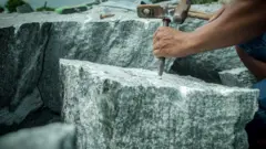 Pedra é quebrada por um trabalhador com auxílio de uma marreta