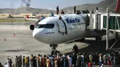 People clamber on top of planes as smoke rises in the distance