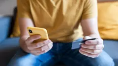 Mãos de um homem segurando celular e cartão de crédito