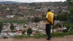 Umugabo ureba agace gatuwemo mu bucucike mu mujyi wa Kigali, gateganye n'inzu zigezweho. Abahatuye bavuze ko ubuyobozi bw'umujyi bushaka kuhabimura ku gahato nta ngurane hagahabwa umushoramari ngo ahubake inzu zigezweho - ibyo umujyi wa Kigali uhakana. (Ifoto yo mu bubiko)