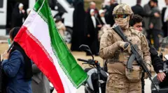 Un efectivo de la Guardia Revolucionaria en Teherán sostiene un fusil automático junto a una mujer que porta una bandera de Irán