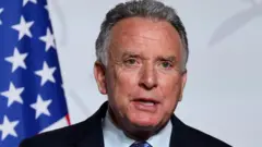 O enviado especial dos EUA para o Oriente Médio, Steve Witkoff, discursando em frente à bandeira americana visível à esquerda.