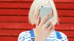 Perempuan memegang ponsel pintar di depan mukanya