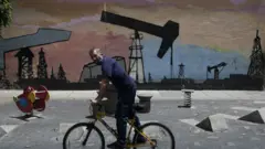 A person on a bike rides past graffiti depicting an oil drilling operation in Caracas in 2020.
