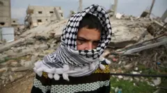 صورة للطفل الفلسطيني سعيد عبد الغفور وهو يلف وجهه بالكوفية الفلسطينية، بعد أن فقد إحدى عينيه في انفجار ذخيرة، أمام أنقاض مبنى مدمر في خان يونس جنوب قطاع غزة، 10 فبراير/شباط 2025.
