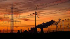 Esta fotografía, tomada al atardecer del 12 de noviembre de 2025, muestra aerogeneradores y postes de luz mientras se elevan los humos de las torres de refrigeración de la central termoeléctrica de lignito operada por el gigante energético alemán RWE, cerca de Neurath, en el oeste de Alemania.