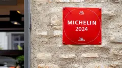 A foto mostra uma parede com uma placa vermelha escritosport 365branco "Michelin 2024". 