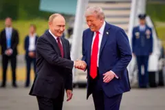 Vladimir Putin e Donald Trump se cumprimentam sorrindo, durante um encontro em 2025