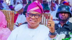 Bọla Oyebamiji wa nibi apero kan to si na ọwọ osi soke, ọlọpaa kan wa lẹyin rẹ.