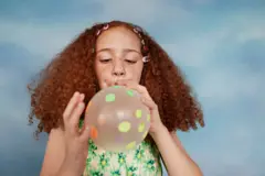 Una niña infla un globo con puntos en su superficie.