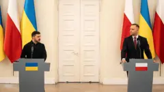 Серйозні Зеленський і Навроцький стоять за трибунами під час пресконференції на відстані кількох метрів. На задньому плані видно закриті білі двері та вертикально розташовані прапори Польщі та України.