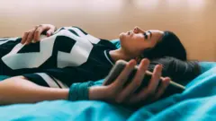 A teenager lying on her bed at home