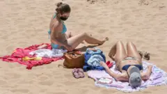 A beachgoer wears her protective mask as she sunbathes