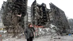 Nurse Svetlana Savchenko stands next to the destroyed building where her apartment was located in Mariupol