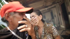 Um homem e uma mulher cobrem os rostos com as mãos em área externa de casa, tentando se proteger de fumaça
