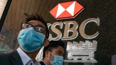 兩名戴著口罩的路人走過香港某匯豐銀行分行（19/2/2020）