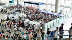 Centenas de pessoas em aeroporto, subindo escadas rolantes e passando por catracas