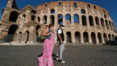 Dos personas con mascarilla frente al Coliseo de Roma.