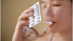 Mujer tomando una pastilla con un vaso de agua.
