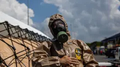Pessoa toda coberta com jaleco e máscara