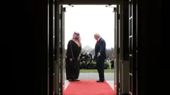 Kapıdan dışarısı görünüyor, kırmızı halının sonunda Trump Suudi prensini içeri davet ediyor. Kasım 2025. 