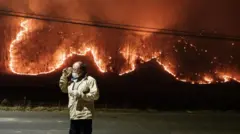 Мужчина разговаривает со своим сыном по телефону перед своим домом во время лесных пожаров в Ыйсоне, Южная Корея, 24 марта 2025 года