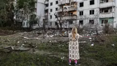 Женщина смотрит на поврежденный дом.