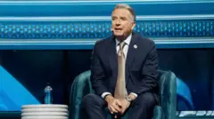 Стів Віткофф у синьому костюмі і картатій краватці сидить у кріслі на голубому фоні 