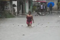 Una mujer con el agua hasta las rodillas camina en una calle inundada en República Dominicana