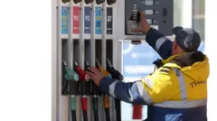Співробітник АЗС у Москві в жовтій фірмовій куртці зі світловідбивними смужками стоїть біля кранів із бензином спиною до об'єктива