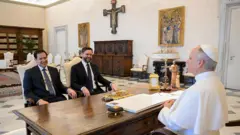 O Papa Leão 14 encontra-se com o vice-presidente dos Estados Unidos, JD Vance, e o secretário de Estado, Marco Rubio, em 19 de maio de 2025, na Cidade do Vaticano. Os dois estão sentados diante dele, com a mesa papal os separando. O Papa veste sua tradicional túnica branca, enquanto Rubio e Vance usam ternos.