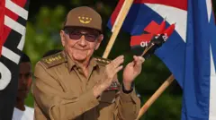 Raul Castro kahverengi askeri üniformasıyla küba bayrağı önünde alkışlıyor