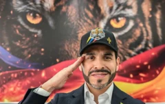 Foto do presidente eleito da Colômbia, Abelardo De la Espriella, usando um boné preto e batendo continência diante da imagem de um tigre estampado na parede