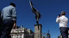 Personas tomando imágenes de la estatua con sus teléfonos celulares.