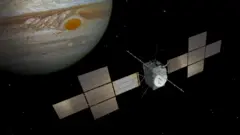 Ilustração da espaçonave Juice, com instrumentos e antenas no meio, ladeados por 'asas' de painéis solares de cada lado, voando no espaço com o planeta Júpiter ao fundo