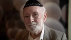 Homem idoso com quipá na cabeça, barba branca e terno.