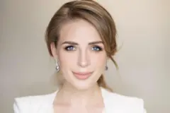 Mulher sorri com o cabelo para trás, vestindo jaqueta branca