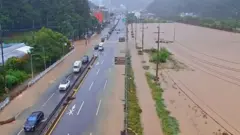 3車線の幹線道路の一部が茶色い水で覆われ、複数の車両が冠水していない車線を1列になって走行している。写真左側は緑の木々が生い茂り、右側一帯は茶色い水で覆われている