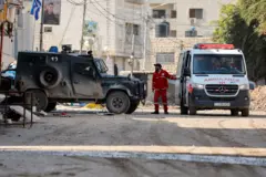 رجل يقف بين سيارة إسعاف ومركبة عسكرية إسرائيلية في جنين بالضفة الغربية المحتلة، 29 يناير/كانون الثاني 2025