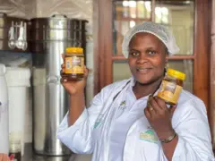 Mme Deborah Nzarubara, Directrice de Grecom, tient deux boites de miel dans les deux mains et elle est vêtue d'une blouse blanche.