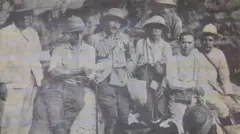 Siete hombres en trajes de exploradores y sombreros de safari posan frente a la cámara recostados sobre una roca