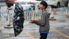 Un adolescente con paraguas camina por la calle bajo una intensa lluvia